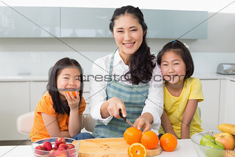 Woman with happy two daughters cutting fruit in kitchen