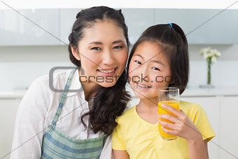 Girl holding orange juice with her mother in kitchen