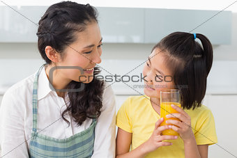 Young girl holding orange juice with her mother in kitchen