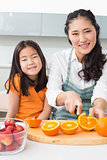 Woman with her young daughter cutting fruit in kitchen