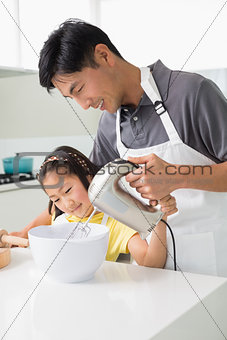 Man with daughter using electric whisk into bowl in kitchen