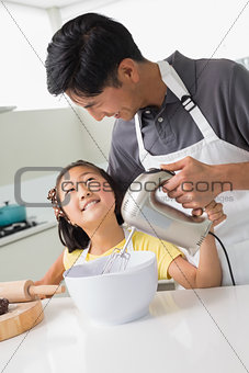 Man with his daughter using electric whisk into bowl in kitchen