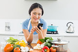 Woman text messaging in front of vegetables in kitchen