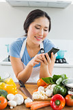 Woman text messaging in front of vegetables in kitchen