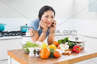 Woman using mobile phone in front of vegetables in kitchen