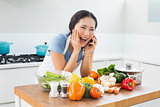 Woman using mobile phone in front of vegetables in kitchen