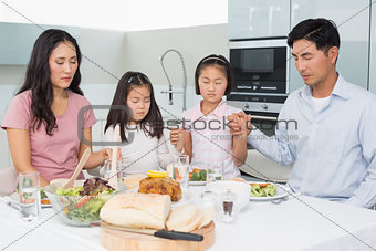 Family of four saying grace before meal in kitchen