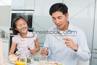 Little girl watching father eat food with a fork in kitchen