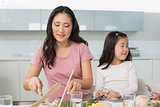Little girl and mother eat food in kitchen