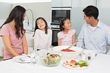 Smiling family of four sitting at dining table in kitchen