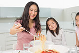 Girls watching happy woman serve spaghetti in kitchen