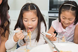 Two happy kids enjoying spaghetti lunch in kitchen