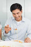 Happy young man enjoying spaghetti lunch in kitchen