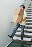 Young man carrying boxes against staircase