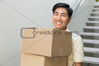Smiling young man carrying boxes against staircase