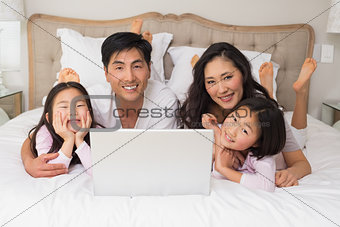 Happy relaxed family of four using laptop in bed