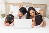 Happy family of four using laptop in bed