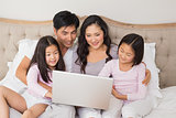 Relaxed family of four using laptop in bed
