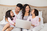 Relaxed family of four using laptop in bed