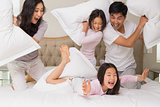 Family of four having pillow fight on bed