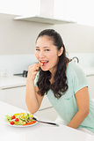 Portrait of a young woman eating salad in kitchen