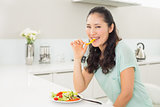 Portrait of a young woman eating salad in kitchen