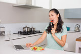 Young woman with laptop eating salad in kitchen