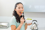 Side view of a young woman eating salad in kitchen