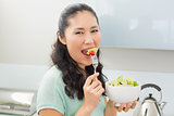 Side view portrait of a woman eating salad in kitchen