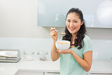 Smiling young woman eating cereals in kitchen