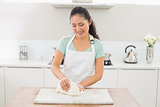 Smiling young woman kneading dough in kitchen