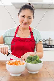 Smiling young woman chopping vegetables in kitchen
