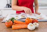 Mid section of a woman with recipe book and vegetables in kitchen