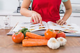 Mid section of a woman with recipe book and vegetables