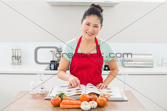 Smiling woman with recipe book and vegetables in kitchen