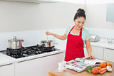 Woman looking at recipe book and preparing food in kitchen