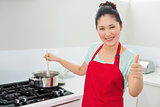 Woman preparing food while gesturing thumbs up in kitchen