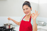 Woman preparing food while gesturing okay sign in kitchen