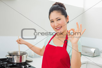 Woman preparing food while gesturing okay sign in kitchen