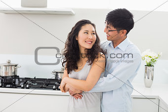 Smiling man embracing woman from behind in kitchen