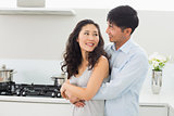 Smiling man embracing woman from behind in kitchen
