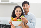 Young couple holding bowl full of fruit in kitchen