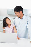Smiling father with young daughter using laptop in kitchen