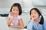 Two smiling young girls with laptop in kitchen