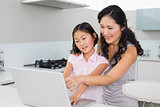 Smiling mother with young daughter using laptop in kitchen