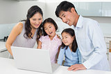 Happy family of four using laptop in kitchen