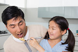 Young daughter feeding cereals to father in kitchen