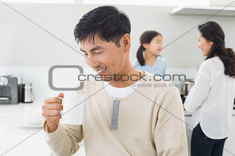Smiling man drinking coffee with family in background