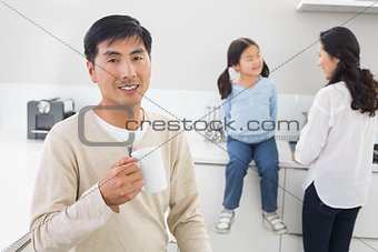 Smiling man holding coffee cup with family in background