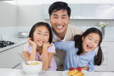 Smiling man with happy daughters having breakfast in kitchen